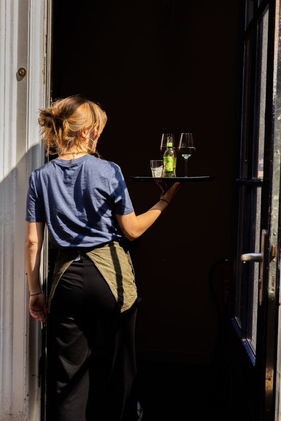 Achterkant van medewerker van Loev Deventer die de horecazaak in loopt met een dienblad.